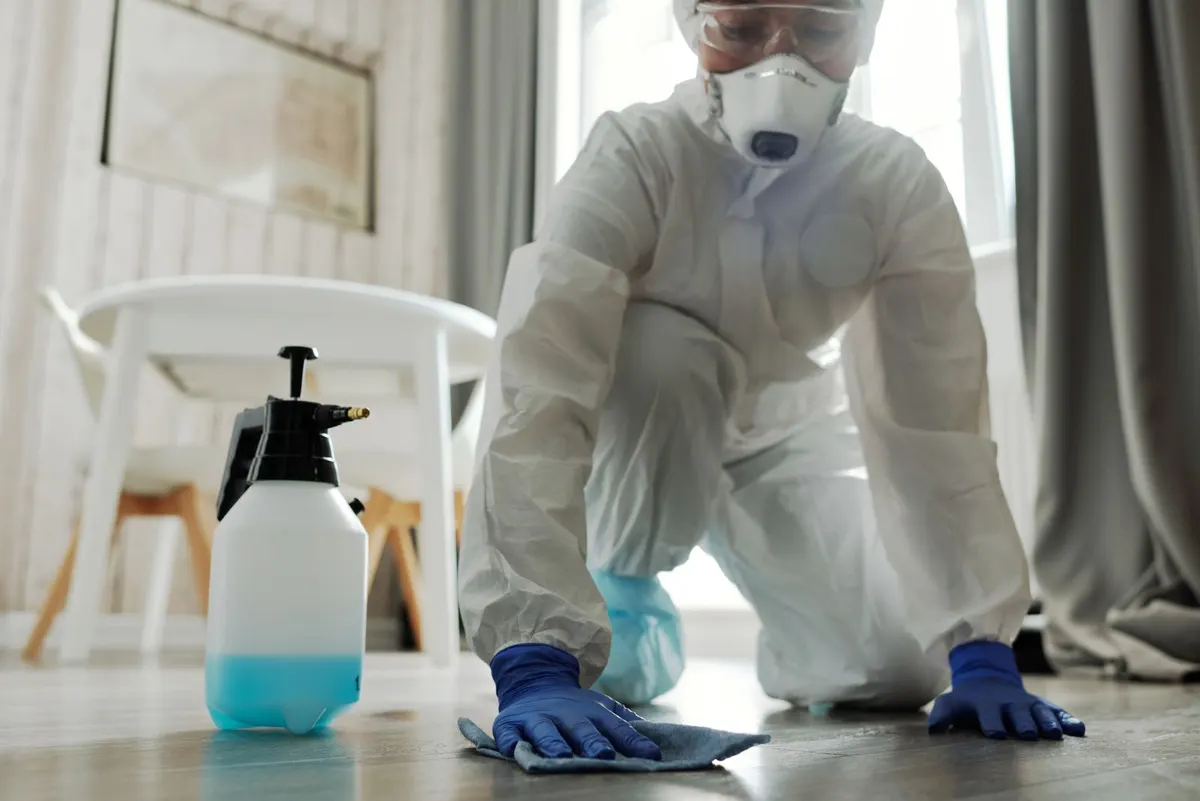 Schoonmaker in beschermende kleding maakt de vloer van een woning schoon