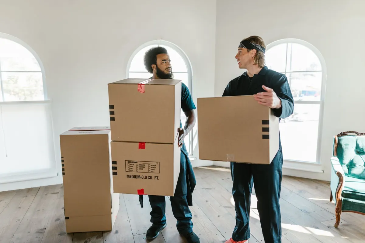 Twee mannen dragen verhuisdozen door een lichte, lege kamer